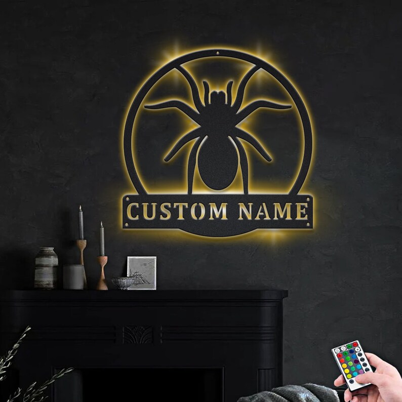 May include: A black metal wall decor with a spider silhouette and a customizable nameplate. The decor is illuminated with warm white LED lights and comes with a remote control for color changing.