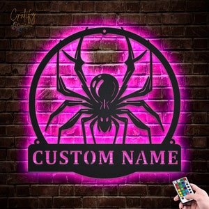 Może przedstawiać: Czarna metalowa sylwetka pająka z jarzącym się r&oacute;żowym halo i spersonalizowaną tabliczką z napisem "CUSTOM NAME".