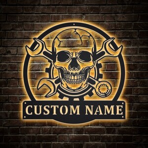 May include: Black metal wall art featuring a skull with crossed wrenches and the text "CUSTOM NAME".