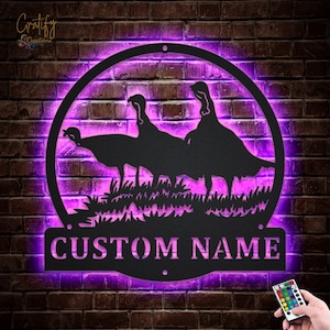 May include: A black metal silhouette of three turkeys in a circular frame with a custom nameplate. The frame is illuminated with purple LED lights. The nameplate reads "CUSTOM NAME".