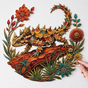Pode incluir: Uma peça de arte de parede circular com um lagarto-de-chifres texturizado e multicolorido pousado num tronco, rodeado por uma coroa de flores vibrantes vermelhas, laranjas, amarelas e azul-petróleo com folhagem verde, em estilo mosaico.