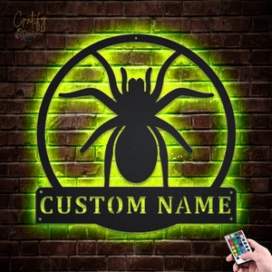 May include: A black metal spider silhouette with a custom nameplate, illuminated with a green light. The spider is in a circle with a web design.