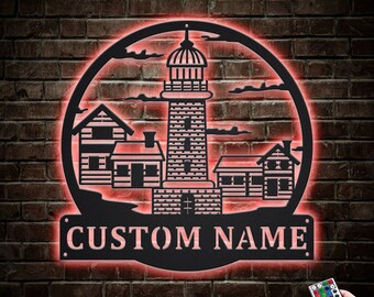 Könnte beinhalten: Eine schwarze Metall-Silhouette eines Leuchtturms mit drei kleineren Häusern, die alle mit rotem Licht beleuchtet sind. Der Text "CUSTOM NAME" wird unter dem Leuchtturm angezeigt. Eine Fernbedienung mit mehreren farbigen Knöpfen ist in der unteren rechten Ecke sichtbar.