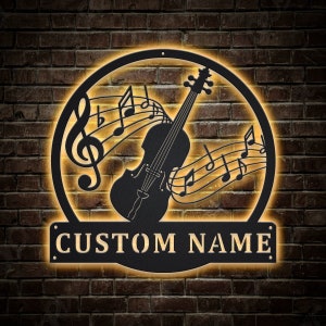 May include: Black metal wall art featuring a violin with musical notes and a custom nameplate. The art is illuminated with warm yellow light.