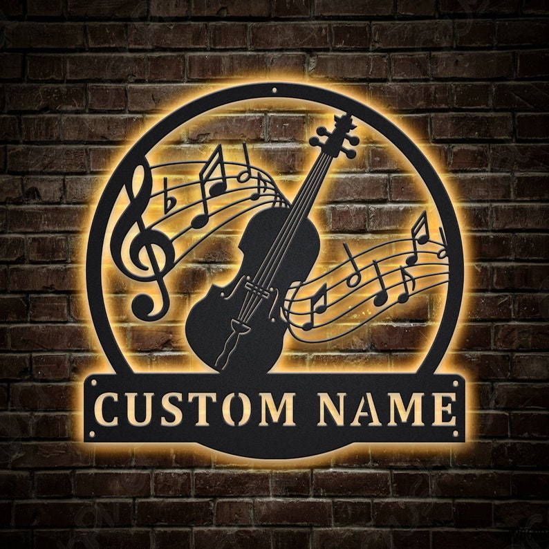 May include: Black metal wall art featuring a violin with musical notes and a custom nameplate. The art is illuminated with warm yellow light.