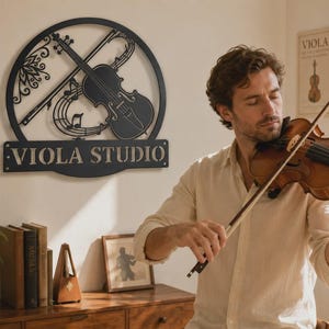 Puede incluir: Un letrero de pared de metal negro con un marco circular que presenta un dise&ntilde;o recortado de un viol&iacute;n, un arco y notas musicales, con el texto VIOLA STUDIO mostrado en una base rectangular en la parte inferior del marco.