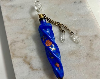 May include: A blue glass bottle with a gold chain and clear glass accents. The bottle is decorated with pink and gold floral designs.