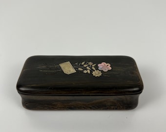 May include: A dark brown rectangular box with a floral design on the lid. The box features a small tag and delicate flowers in pink, white, and gold. The box is likely used for storing small items.