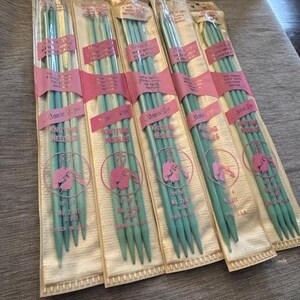 May include: Several packages of vintage knitting needles are displayed. The needles are a pale green color and are packaged in clear plastic with pink labels. The labels feature a graphic of a person knitting. The packages are labeled "Marie Lee Knitting Needles."