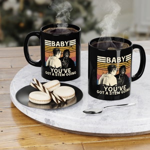 Peut inclure: Deux tasses à café noires avec un design rétro représentant une scène du film "Baby, You've Got a Stew Going". Les tasses ont un texte blanc qui dit "Baby You've Got a Stew Going".