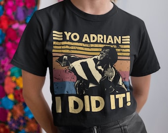 May include: Black t-shirt with a vintage-style graphic of a man with a raised fist and the text "YO ADRIANE I DID IT!"