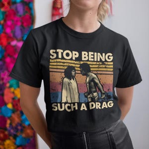 May include: Black t-shirt with a vintage-style graphic featuring two people and the text "Stop Being Such A Drag".