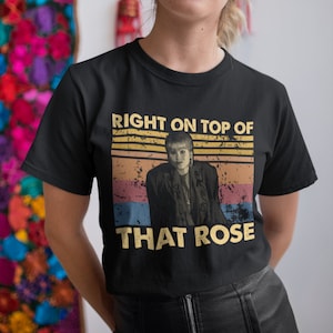 Puede incluir: Camiseta negra con un gráfico de estilo vintage de una mujer con cabello rubio y el texto "RIGHT ON TOP OF THAT ROSE".