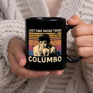 May include: Black ceramic mug with the text "JUST ONE MORE THING" and "COLUMBO" in a retro design. The mug features a portrait of the character Columbo with a vintage colour scheme of orange, yellow, blue, and red.