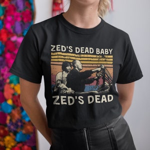 May include: Black t-shirt with a vintage-style graphic of two people riding a motorcycle. The graphic includes the text "Zed's Dead Baby" and "Zed's Dead".