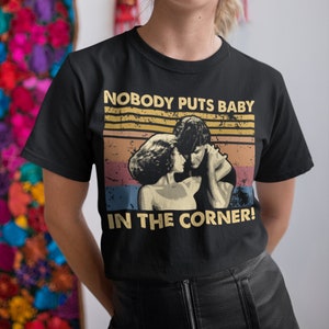 May include: Black t-shirt with a vintage-style graphic of a couple dancing. The graphic features the text "Nobody puts baby in the corner!"