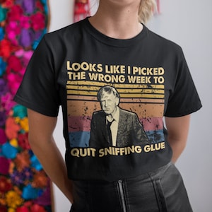 May include: Black t-shirt with a vintage-style graphic featuring a man and the text "Looks like I picked the wrong week to quit sniffing glue."