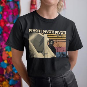 Könnte beinhalten: Schwarzes T-Shirt mit dem Text "PIVOT! PIVOT! PIVOT!". Das Retro-Design zeigt einen Mann, der hinter einem Möbelstück hervorblickt, mit einem Hintergrund in Sonnenuntergangsfarben, orange, gelb und blau.