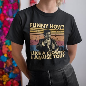 Puede incluir: Camiseta negra con un gráfico de estilo vintage que presenta a un hombre con traje y el texto "Funny how? Like a clown? I amuse you?"
