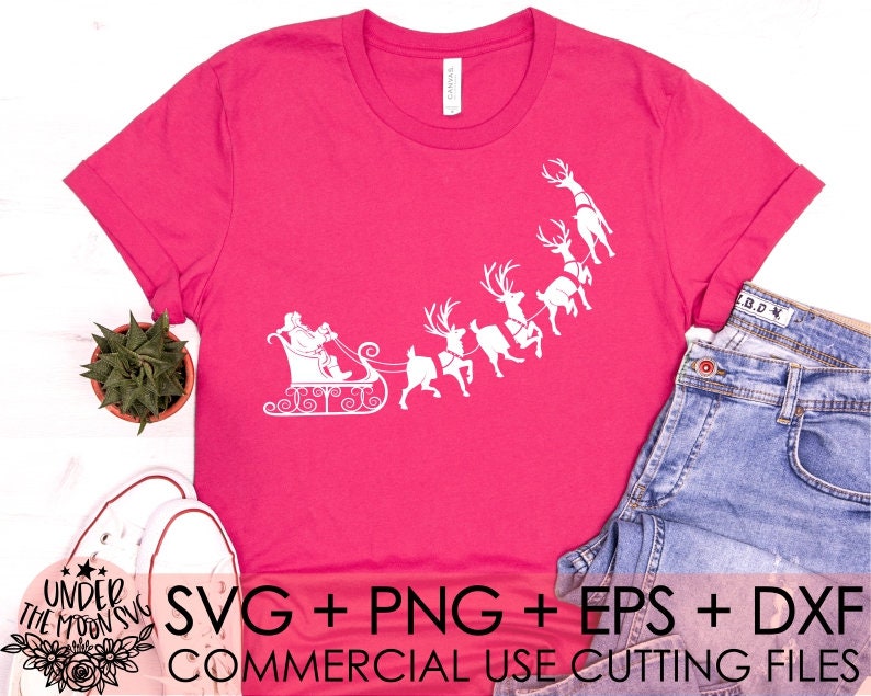 May include: A pink t-shirt with a white design of Santa Claus in a sleigh pulled by reindeer. The text "SVG + PNG + EPS + DXF COMMERCIAL USE CUTTING FILES" is at the bottom of the shirt.