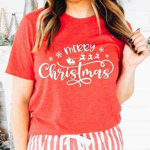 May include: Red t-shirt with white text that says "Merry Christmas" with a graphic of Santa's sleigh and reindeer.