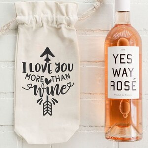 May include: A white canvas wine bag with the text "I love you more than wine" and a black arrow design. A bottle of rose wine with the label "Yes Way Rose" is next to the bag.