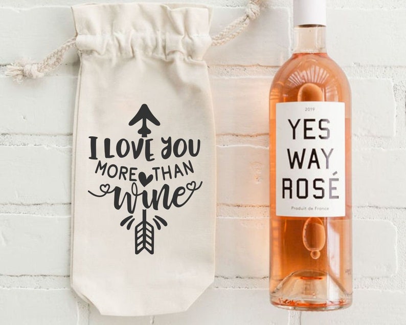 May include: A white canvas wine bag with the text "I love you more than wine" and a black arrow design. A bottle of rose wine with the label "Yes Way Rose" is next to the bag.