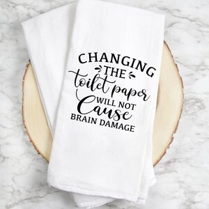 May include: White kitchen towel with black text that reads "Changing the toilet paper will not cause brain damage."