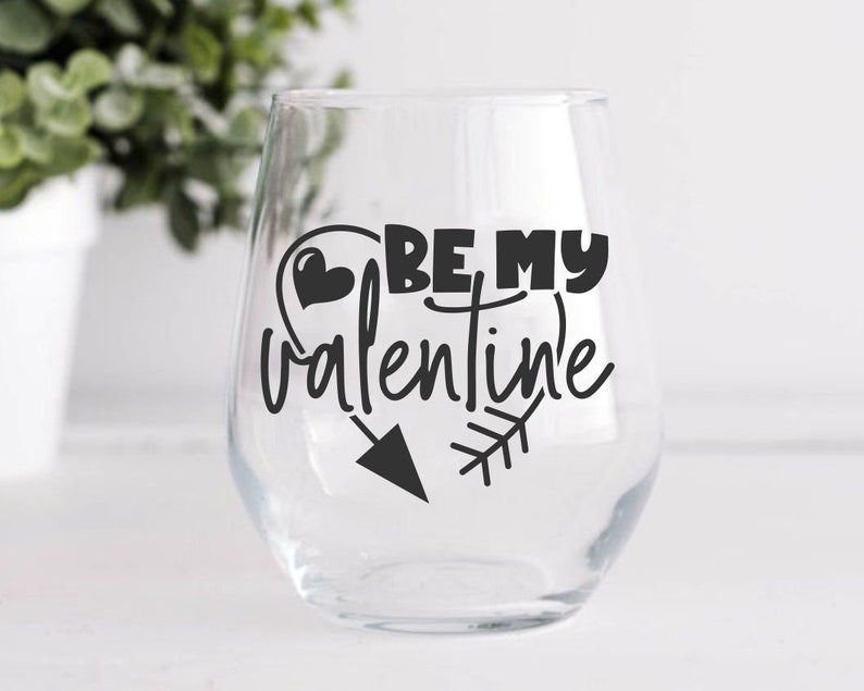 May include: A clear glass wine glass with a black vinyl decal that says "Be My Valentine" with a heart and arrow design.
