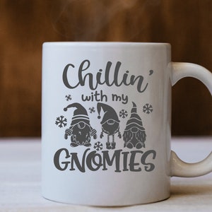 May include: White ceramic mug with a black design that says "Chillin' with my Gnomes". The design includes three gnomes wearing hats and holding presents.