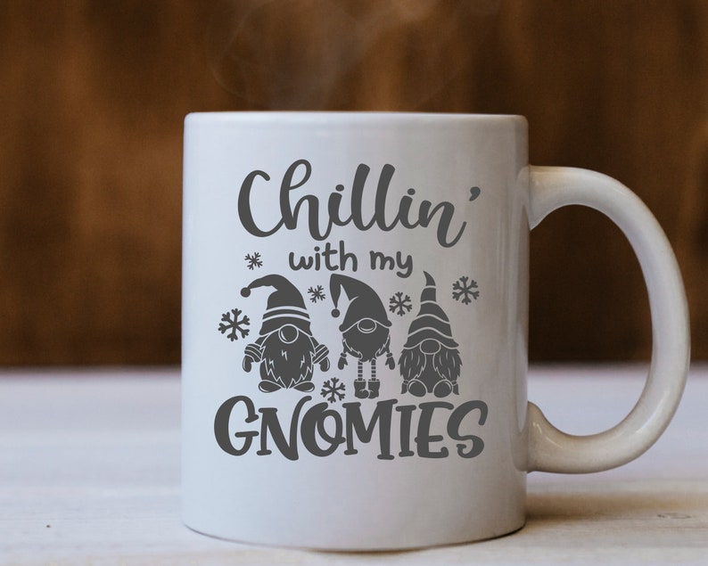 May include: White ceramic mug with a black design that says "Chillin' with my Gnomes". The design includes three gnomes wearing hats and holding presents.