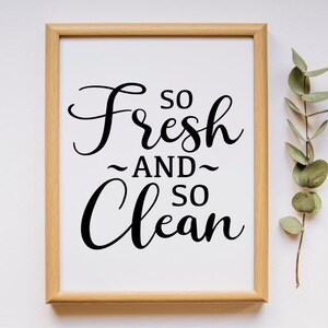 May include: A framed print with the text "So Fresh and So Clean" in a black cursive font on a white background. The frame is light brown wood.