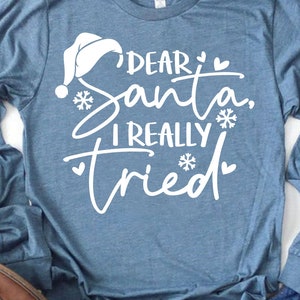 May include: A blue long-sleeved shirt with white text that reads "Dear Santa, I really tried" with a white Santa hat and snowflakes.