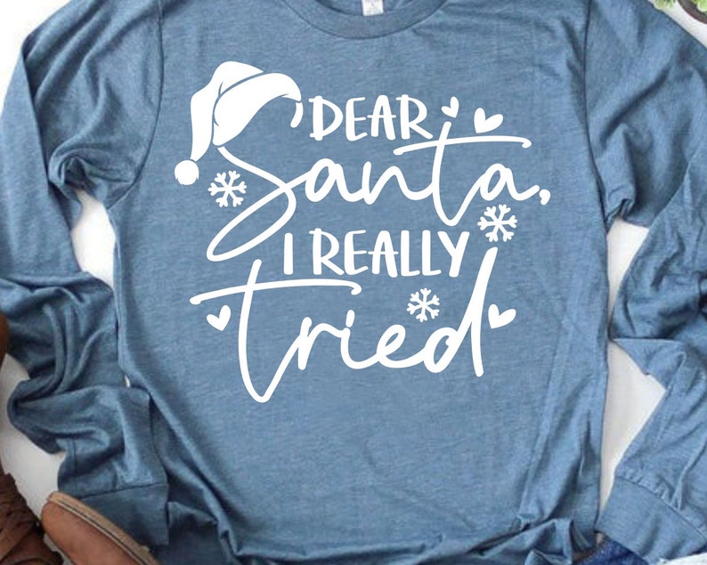 May include: A blue long-sleeved shirt with white text that reads "Dear Santa, I really tried" with a white Santa hat and snowflakes.