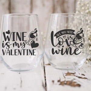 May include: Two clear glass wine glasses with black vinyl lettering. The first glass says "Wine is my Valentine". The second glass says "All you need is love & wine".