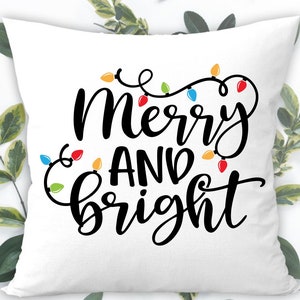 May include: White throw pillow with black text that reads "Merry and Bright" with a string of colorful Christmas lights around the text.