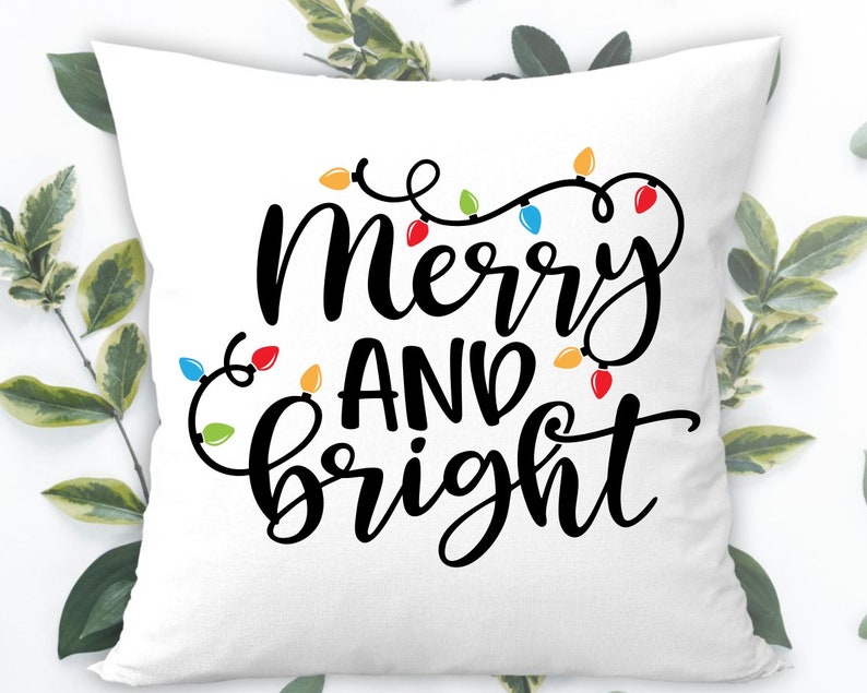 May include: White throw pillow with black text that reads "Merry and Bright" with a string of colorful Christmas lights around the text.
