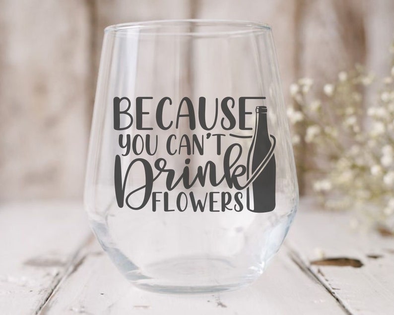 May include: A clear glass wine glass with a black vinyl decal that reads "Because you can't drink flowers". A black silhouette of a wine bottle is next to the text.