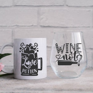 May include: White ceramic mug with a black graphic of a mug with the text "Love Potion" and a white wine glass with the text "Wine not" in black.