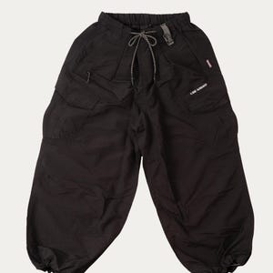 Può includere: Pantaloni cargo neri con più tasche e vita elasticizzata. I pantaloni hanno una chiusura con coulisse e un piccolo logo sulla tasca destra. I polsini inferiori sono raccolti con elastico. Realizzati in materiale leggero.