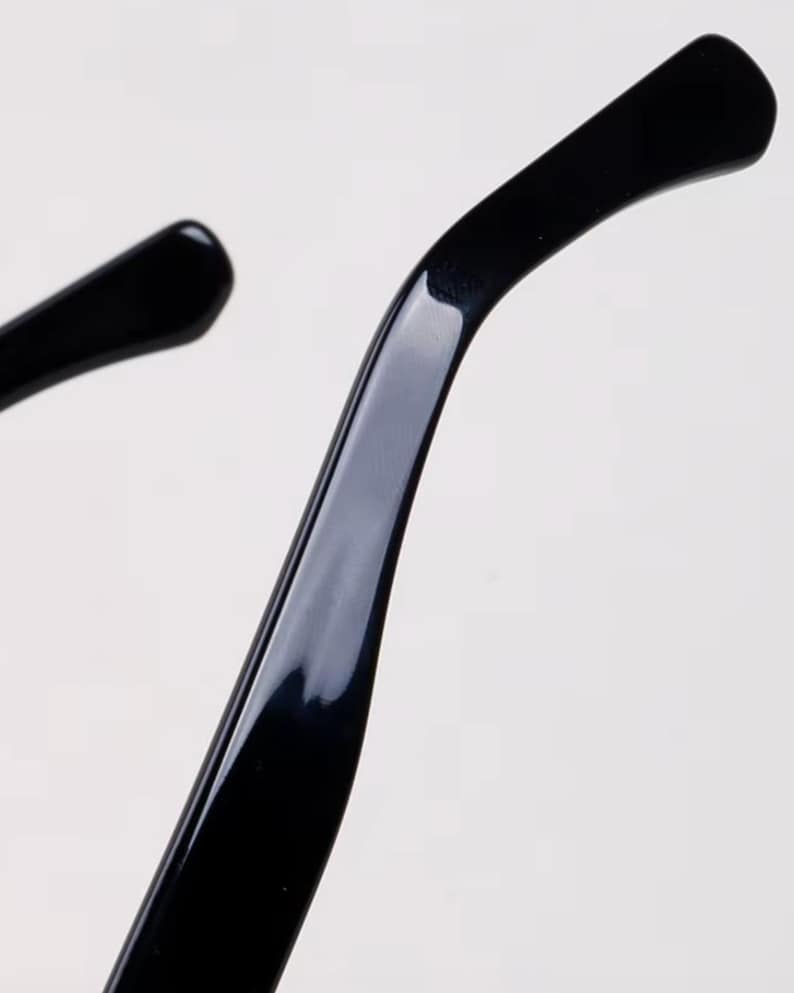 May include: Close-up of the temple arm of black eyeglasses. The arm curves gently and has a glossy finish. The image is set against a plain white background, highlighting the sleek design of the eyewear.