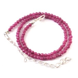 May include: A necklace with small, faceted, ruby-coloured beads. It has a silver-coloured chain and clasp. The beads are strung together, creating a layered effect. This necklace is ideal for adding a touch of colour to any outfit.