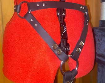 May include: Black leather harness with silver metal accents and a large ring. The harness is worn on a red mannequin.