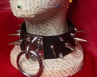 May include: Black leather choker with silver spikes and a large silver ring. The choker is on a mannequin's neck.