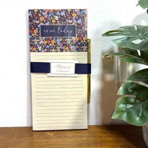 Può includere: Un blocco note floreale con una penna dorata. Il blocco note ha un nastro blu e dice "To Do Today" sul davanti. Il blocco note è etichettato "Lady Jayne List Pad & Pen".