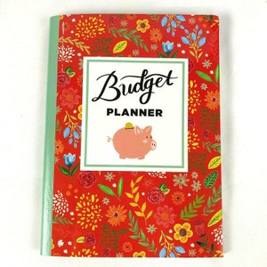May include: A red budget planner with a floral pattern and a piggy bank illustration. The cover says "Budget Planner".