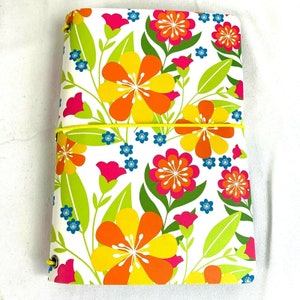 May include: A white notebook cover with a floral pattern featuring yellow, orange, pink, and green flowers. The notebook has a yellow elastic band.
