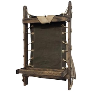 May include: A rustic wooden wall-mounted display shelf with a dark green canvas backing. The shelf has a small tray at the bottom and is laced with rope. The frame is made of dark wood, and the canvas is secured with rope.