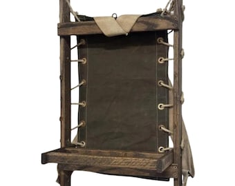 May include: A vintage-style wooden frame backpack featuring a dark olive green canvas panel secured with light-colored rope lacing through metal grommets. The structure includes a wooden base shelf and beige canvas shoulder straps attached to the frame.