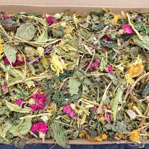 Puede incluir: Una caja de cartón llena de una variedad de hierbas y flores secas. Las hierbas y las flores son una mezcla de verdes, amarillos y rosas.